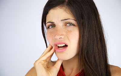 A woman holding the side of her mouth in pain