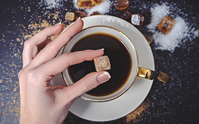 A sugar cube being placed into a cup of coffee