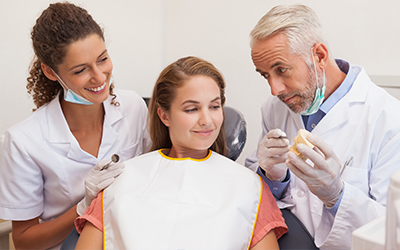 A male dentist and female assistant smiling while talking to a patient in the chair